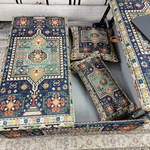 May include: A blue and orange patterned storage ottoman with a hinged top. The ottoman is open and has two patterned throw pillows inside.