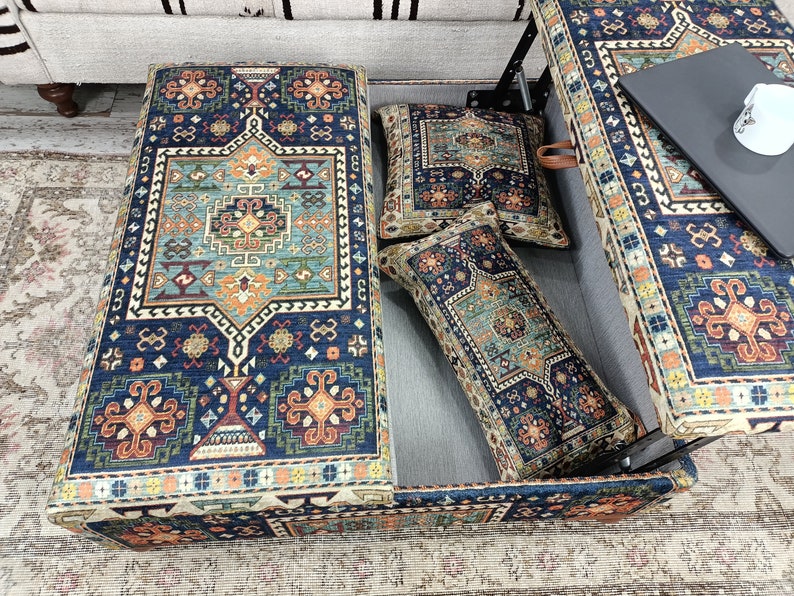 May include: A blue and orange patterned storage ottoman with a hinged top. The ottoman is open and has two patterned throw pillows inside.