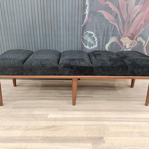 May include: A black upholstered bench with four legs and a wooden frame. The bench is divided into four sections.