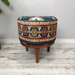 May include: A round, blue ottoman with a colorful geometric pattern. The ottoman has a wooden base with three legs.