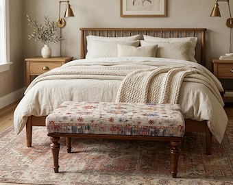 Könnte beinhalten: Ein Schlafzimmer mit einem Holzbett, beiger Bettwäsche und einer gemusterten Bank. Die Bank hat einen dunklen Holzrahmen und ein Blumenmuster. Eine cremefarbene Strickdecke ist über das Bett drapiert. Warme Atmosphäre.