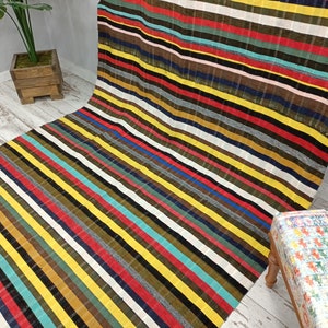 May include: Multicolored striped rug with a variety of colors including red, yellow, blue, green, and brown. The rug is made of a woven fabric and has a soft texture.