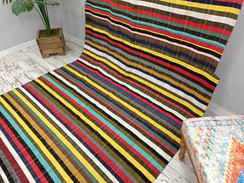May include: Multicolored striped rug with a variety of colors including red, yellow, blue, green, and brown. The rug is made of a woven fabric and has a soft texture.