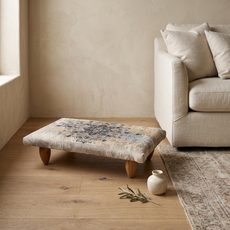 a minimalist living room with a beige sofa, a decorative ottoman, and a small white vase with a plant on the floor.