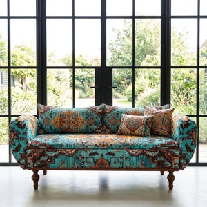 May include: A patterned sofa in turquoise and brown, with matching cushions. The sofa has a curved design and wooden legs. The cushions display similar patterns in orange, brown, and turquoise. The sofa's dimensions are not visible.