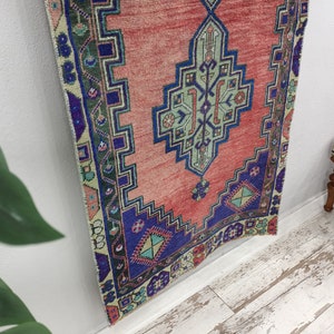 May include: A red, blue, and green patterned rug with a geometric design. The rug is hanging on a white wall.