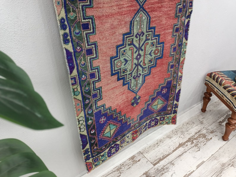 May include: A red, blue, and green patterned rug with a geometric design. The rug is hanging on a white wall.