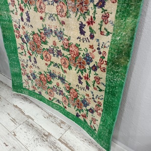 May include: A vintage rug with a floral pattern in shades of pink, green, and white. The rug has a green border and is made of a soft, woven material.