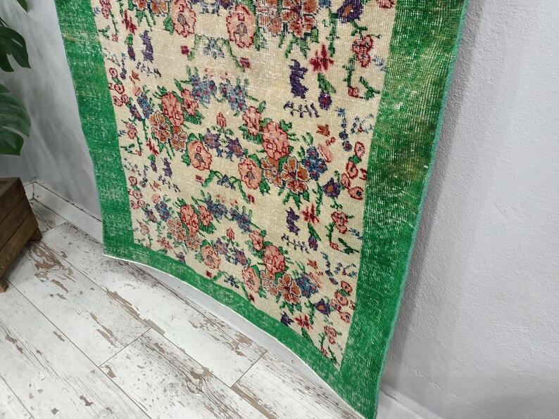 May include: A vintage rug with a floral pattern in shades of pink, green, and white. The rug has a green border and is made of a soft, woven material.