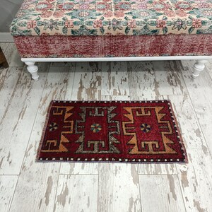 May include: A red, orange, and black patterned rug with a geometric design. The rug is placed on a whitewashed wood floor.