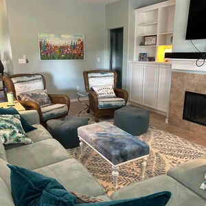 Puede incluir: Una sala de estar con un sof&aacute; azul claro, dos sillones de mimbre, un puf azul y blanco y una mesa de centro blanca con una tapa de patr&oacute;n azul y blanco. La habitaci&oacute;n tiene una pared azul claro con una pintura de flores en ella. Hay una chimenea con un marco de piedra y un televisor de pantalla plana en la pared encima de ella. La habitaci&oacute;n est&aacute; decorada con una alfombra con un patr&oacute;n de helechos.