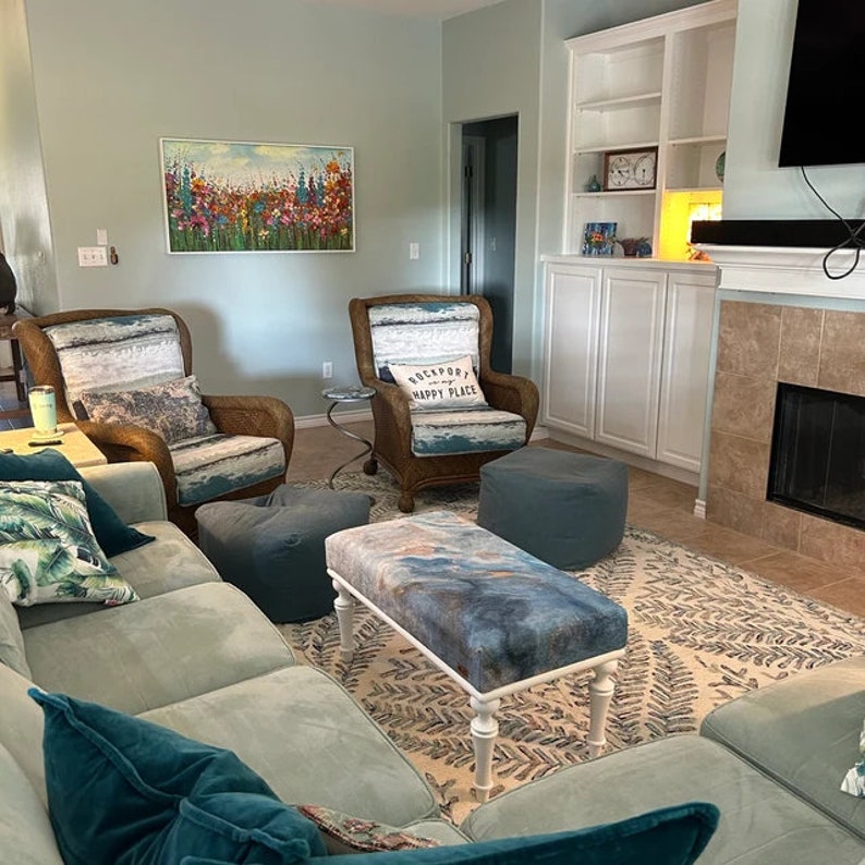 Puede incluir: Una sala de estar con un sof&aacute; azul claro, dos sillones de mimbre, un puf azul y blanco y una mesa de centro blanca con una tapa de patr&oacute;n azul y blanco. La habitaci&oacute;n tiene una pared azul claro con una pintura de flores en ella. Hay una chimenea con un marco de piedra y un televisor de pantalla plana en la pared encima de ella. La habitaci&oacute;n est&aacute; decorada con una alfombra con un patr&oacute;n de helechos.