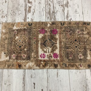 Op de afbeelding: Een vintage Turks tapijt met een beige achtergrond en een geometrisch patroon in tinten bruin, roze en zwart. Het tapijt heeft een verweerde look en is perfect om een ​​bohemien touch aan je huis toe te voegen.