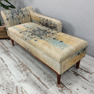 Könnte beinhalten: Eine beige Chaiselongue mit gemustertem Stoffbezug in Blau, Grün und Gelb. Die Chaiselongue hat Holzbeine und eine geschwungene Rückenlehne.