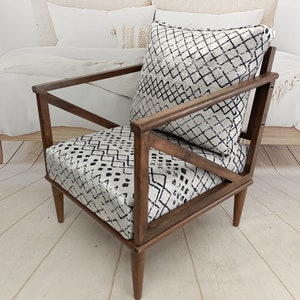 May include: A brown wooden armchair with a black and white geometric patterned cushion and fabric upholstery.
