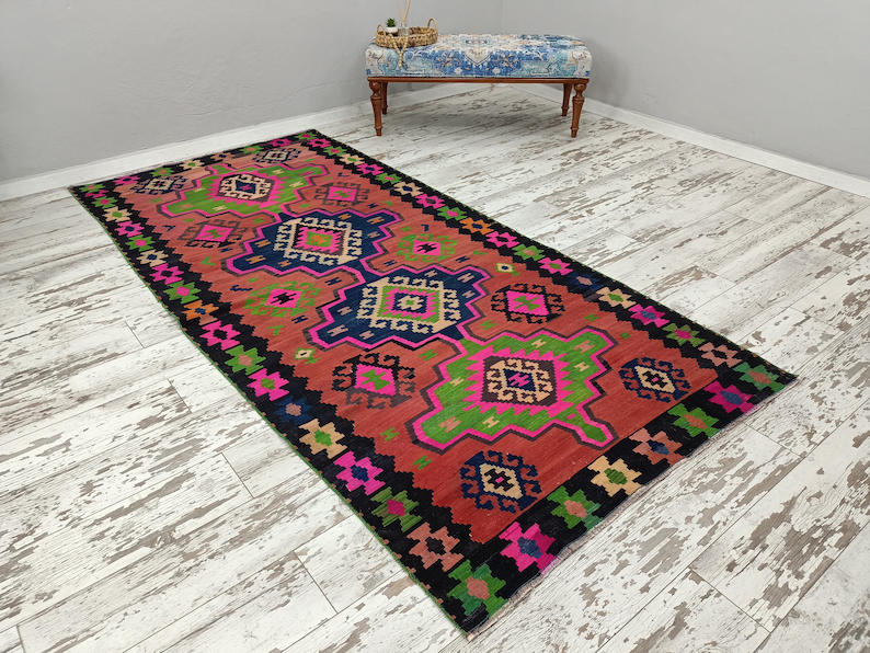 Puede incluir: Una alfombra colorida con un patr&oacute;n geom&eacute;trico en tonos de rosa, verde, azul y negro. La alfombra tiene un dise&ntilde;o tradicional con detalles intrincados.
