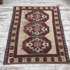 May include: A vintage rug with a cream background and a red, blue, and green geometric pattern. The rug has a border with a repeating pattern of diamonds and stars.