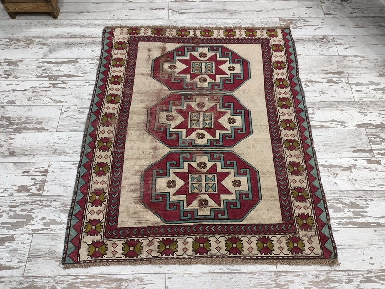 May include: A vintage rug with a cream background and a red, blue, and green geometric pattern. The rug has a border with a repeating pattern of diamonds and stars.