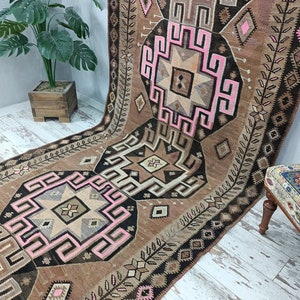 May include: A vintage Turkish rug with a brown, black, and pink geometric pattern. The rug has a traditional design with intricate details and a faded, worn look.