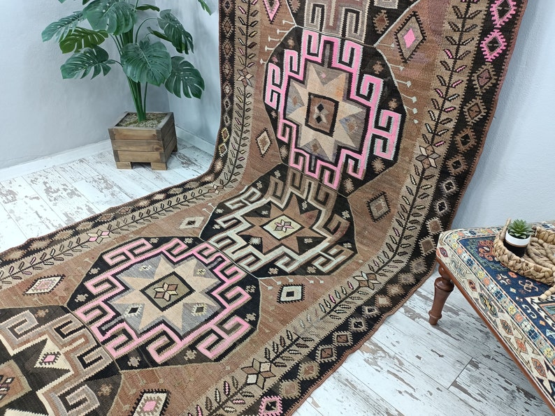 May include: A vintage Turkish rug with a brown, black, and pink geometric pattern. The rug has a traditional design with intricate details and a faded, worn look.