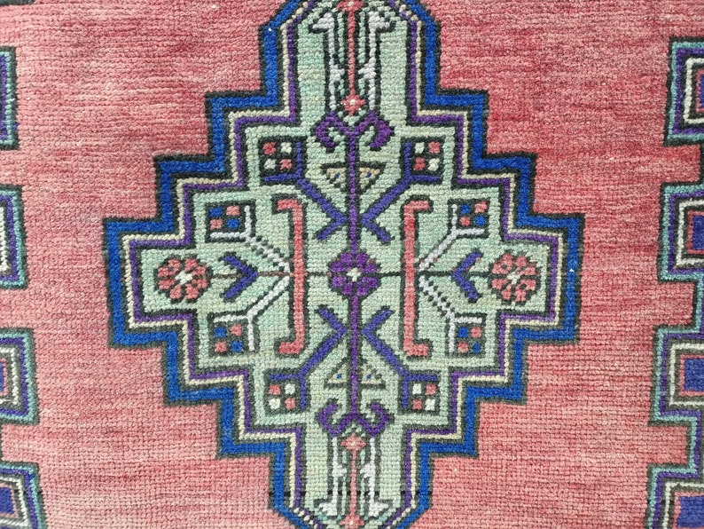 May include: A close-up of a red rug with a detailed blue, green, and purple geometric pattern in the center.
