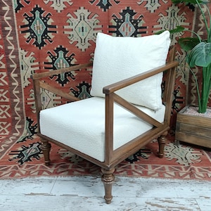 May include: A white upholstered armchair with a wooden frame and turned legs. The chair has a white cushion and is sitting on a red and black patterned rug.