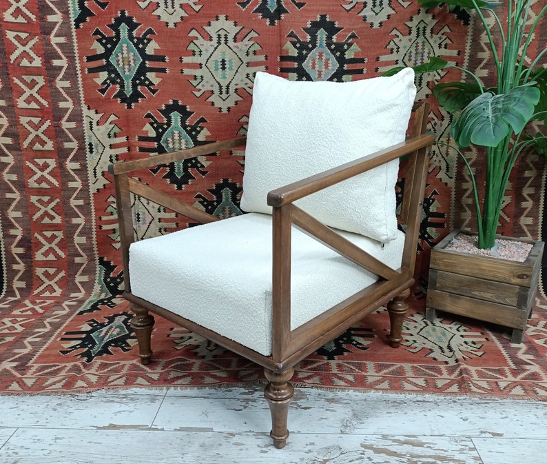 May include: A white upholstered armchair with a wooden frame and turned legs. The chair has a white cushion and is sitting on a red and black patterned rug.