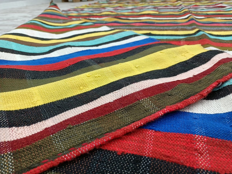 May include: A colorful striped woven rug with a variety of colors including red, yellow, blue, green, and black.