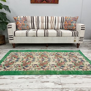 May include: A vintage floral patterned rug with a green border. The rug is laid out on a white wood floor in front of a white sofa with striped cushions.
