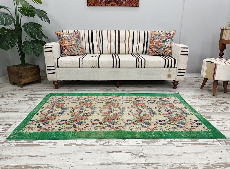 May include: A vintage floral patterned rug with a green border. The rug is laid out on a white wood floor in front of a white sofa with striped cushions.