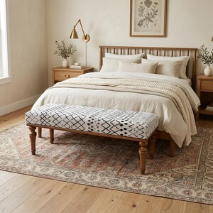 Peut inclure: Une chambre à coucher avec un lit en bois, une literie aux tons neutres et un banc à motifs géométriques noirs et blancs. Le banc est placé au pied du lit. Un tapis d'aspect vintage et délavé est sous le lit et le banc.