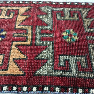 May include: Close-up of a red, orange, and gray patterned rug with a geometric design. The rug has a fringe border.
