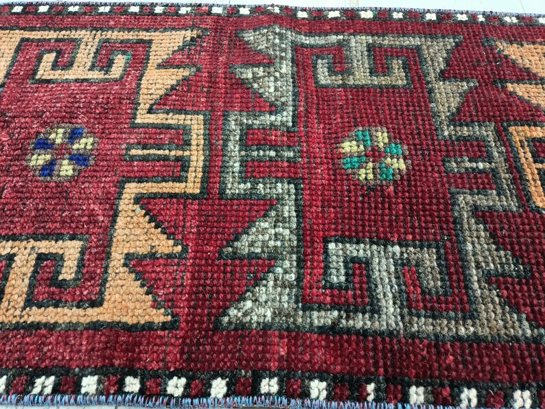 May include: Close-up of a red, orange, and gray patterned rug with a geometric design. The rug has a fringe border.