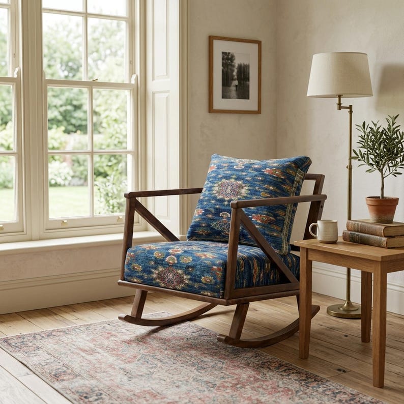 A cozy corner of a room with a wooden rocking chair, a small side table with a lamp, and a potted plant. The room has a large window that provides a view of the outdoors, and the overall decor has a vintage, rustic feel.