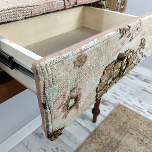 Op de afbeelding: Een houten bijzettafel met een lade. De lade is open en bekleed met een stoffen patroon. De ladegreep is een gouden ring.