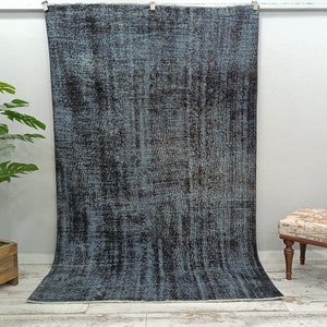 May include: A blue and black distressed rug with a faded, vintage look. The rug is hanging on a wall and has a textured surface.