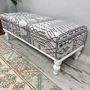 May include: White storage bench with a black and white geometric patterned fabric top and turned wooden legs.