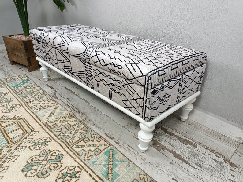 May include: White storage bench with a black and white geometric patterned fabric top and turned wooden legs.