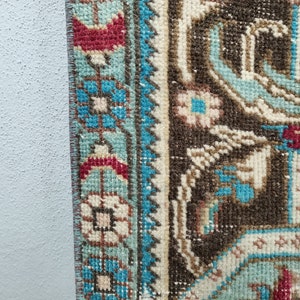 May include: Close-up of the edge of a brown and blue patterned rug with a fringe. The rug has a floral design with white, blue, and red accents.