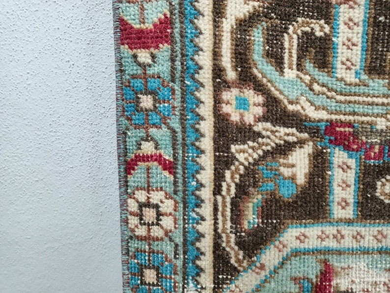 May include: Close-up of the edge of a brown and blue patterned rug with a fringe. The rug has a floral design with white, blue, and red accents.
