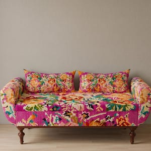 May include: A vibrant, patterned loveseat with two matching throw pillows. The sofa features a bright pink background with a colorful floral design in shades of orange, yellow, green, and blue. The wooden legs add a touch of elegance.