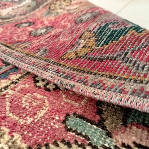 May include: Close-up of a pink, blue, and brown patterned rug with a detailed woven edge.