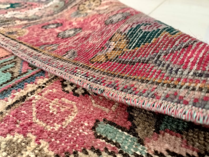 May include: Close-up of a pink, blue, and brown patterned rug with a detailed woven edge.