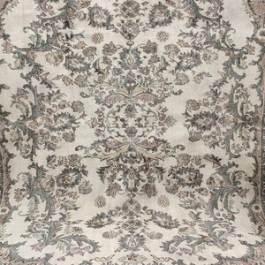 May include: A vintage cream-coloured rug with a floral pattern in shades of brown and green. The rug has a border with a geometric design.