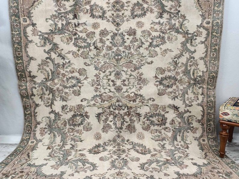 May include: A vintage cream-coloured rug with a floral pattern in shades of brown and green. The rug has a border with a geometric design.