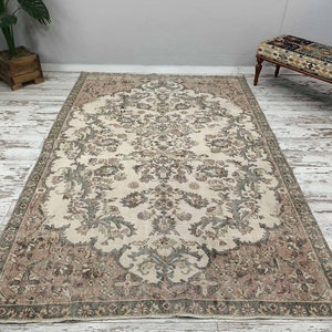 May include: A vintage cream-coloured rug with a floral pattern in shades of brown and green. The rug has a detailed border with a repeating design.