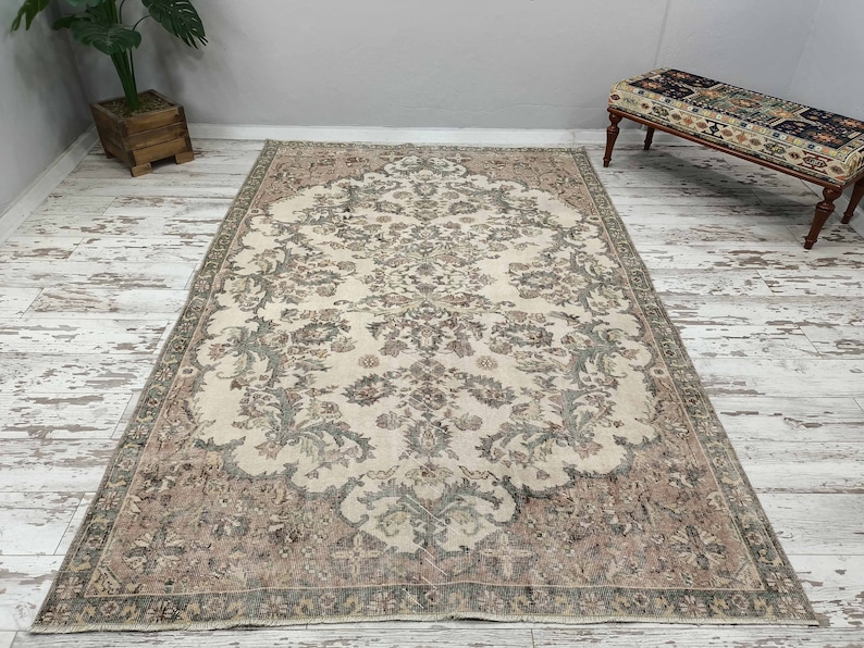May include: A vintage cream-coloured rug with a floral pattern in shades of brown and green. The rug has a detailed border with a repeating design.
