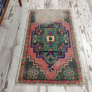 Peut inclure: Un tapis turc vintage avec un motif g&eacute;om&eacute;trique traditionnel dans des tons de vert, rose, bleu et jaune. Le tapis a un aspect vieilli avec des bords effiloch&eacute;s et une apparence us&eacute;e.