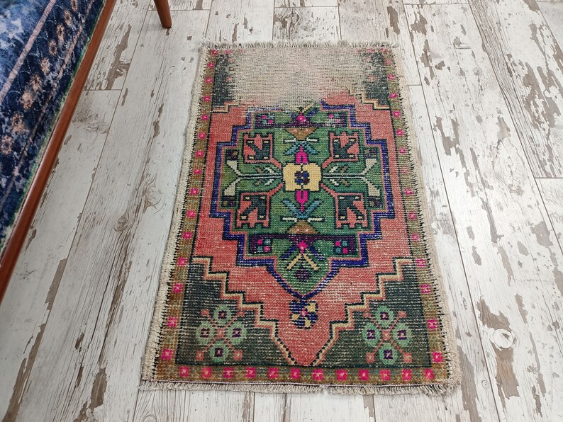 Peut inclure: Un tapis turc vintage avec un motif g&eacute;om&eacute;trique traditionnel dans des tons de vert, rose, bleu et jaune. Le tapis a un aspect vieilli avec des bords effiloch&eacute;s et une apparence us&eacute;e.