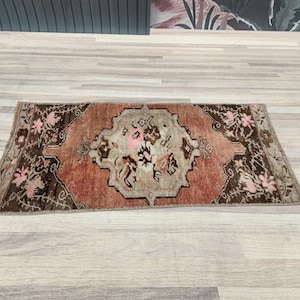 May include: A small, rectangular rug with a brown and pink floral pattern. The rug has a faded, vintage look and is perfect for adding a touch of bohemian style to any room.
